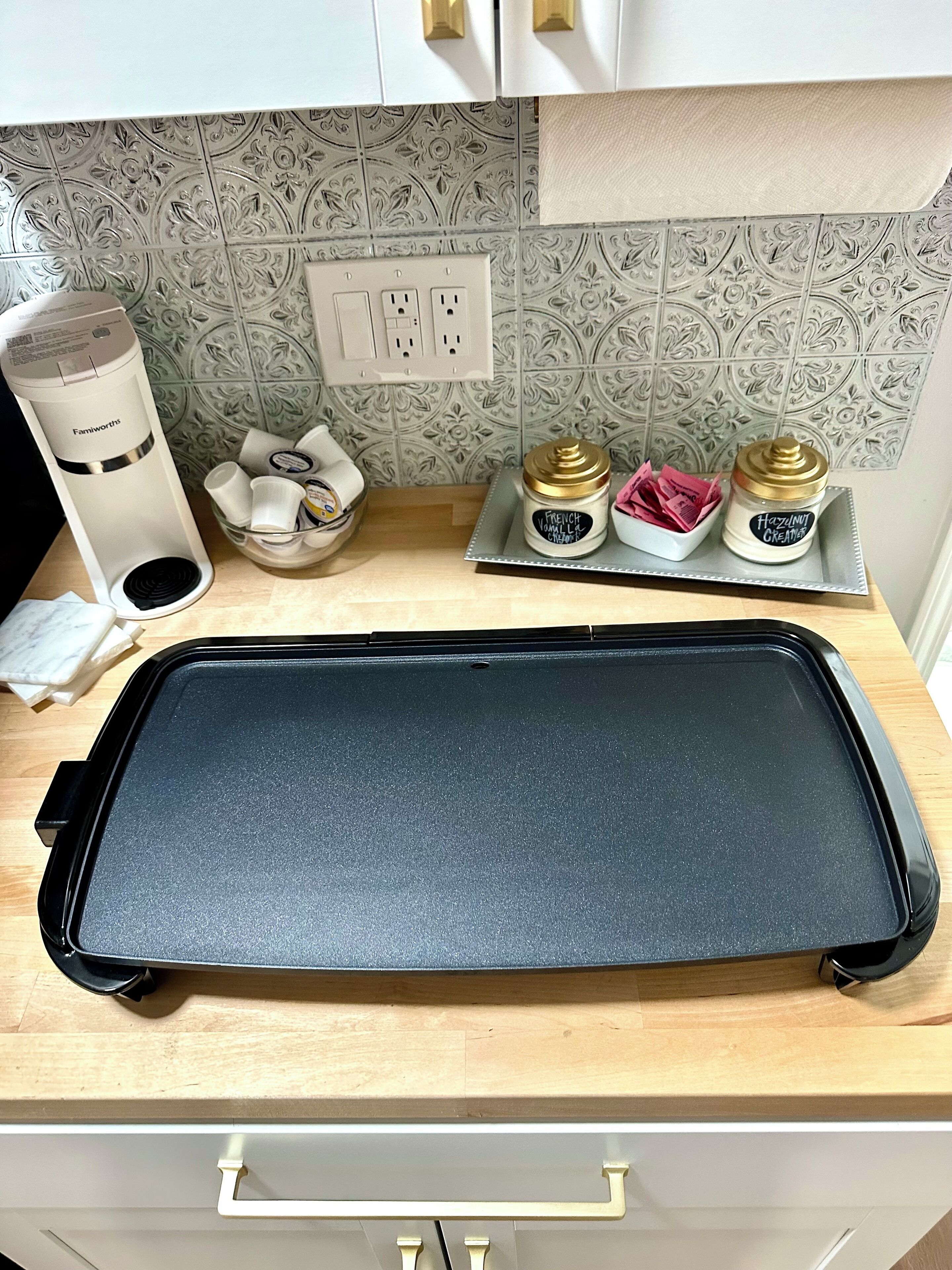 A kitchen counter with a black baking tray, a Famiworth coffee machine, and two containers of French vanilla and hazelnut cream.