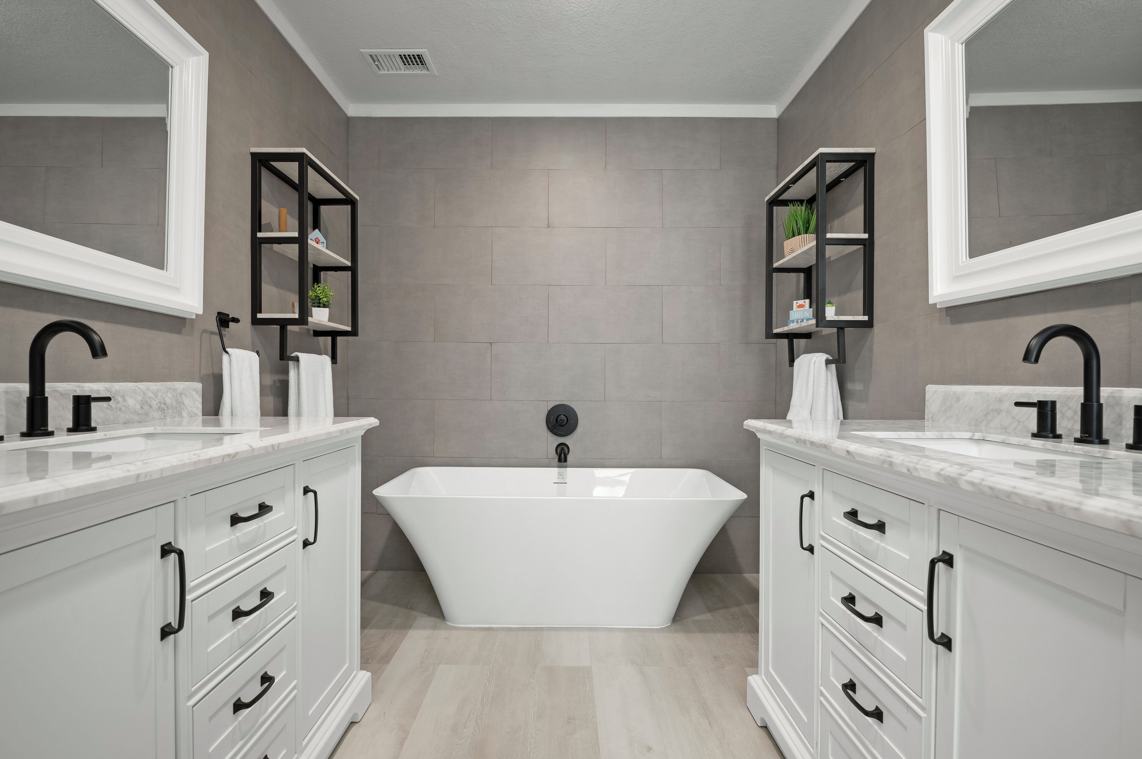 A modern bathroom with a freestanding bathtub, white cabinetry, and black fixtures.