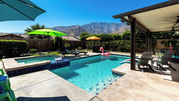 Une piscine avec vue sur les montagnes, entourée de meubles de jardin et de parasols.