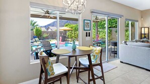 Un espace repas comprenant une table et des chaises, un lustre et de grandes fenêtres donnant sur une piscine et des montagnes.