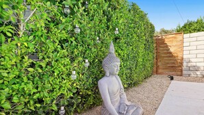 A Buddha statue in a garden with a hedge and a wooden fence. - Modern Palm Springs Pool Home Near Downtown Sleeps 8 (Palm Springs)