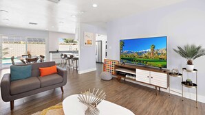 A modern living room with a flat-screen TV, a grey sofa, and a dining area in the background. - Modern Palm Springs Pool Home Near Downtown Sleeps 8 (Palm Springs)