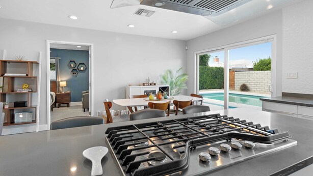 A modern kitchen with a gas stove, dining area with chairs and a table, and a view of a swimming pool. - Modern Palm Springs Pool Home Near Downtown Sleeps 8 (Palm Springs)