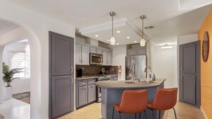 A modern kitchen with grey cabinets, stainless steel appliances, and a central island with two bar stools. - Ranch Club Estates Retreat with Pool and Dog Run (Palm Springs)