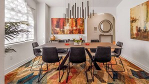 A modern dining area with a long table, black chairs, a colorful rug, and abstract art on the walls. - Ranch Club Estates Retreat with Pool and Dog Run (Palm Springs)