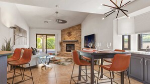 A modern kitchen with a stone fireplace, a dining area with bar stools, and a large window with blinds. - Ranch Club Estates Retreat with Pool and Dog Run (Palm Springs)