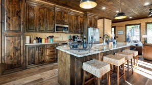 Une cuisine rustique avec des meubles en bois, un îlot central doté de tabourets, un four à micro-ondes et un réfrigérateur.