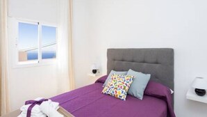 Une chambre à coucher avec un lit, une table de chevet, une fenêtre avec des rideaux et une vue sur la mer.
