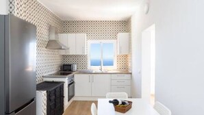 Une cuisine de taille réduite, avec des meubles blancs, un réfrigérateur noir et une fenêtre donnant sur un paysage pittoresque.