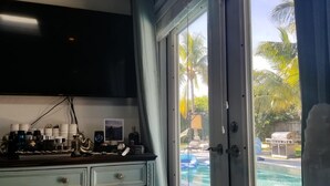 Une chambre dotée d’un mini-bar, d’un téléviseur fixé au mur et offrant une vue sur une piscine bordée de palmiers.