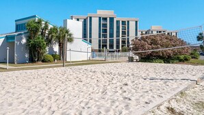 A sandy beach volleyball court with a net, palm trees, and a building in the background. - OCEAN PEARL 2-bedroom condo in peaceful Destin  (Destin)