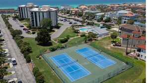 An aerial view of a residential area with two tennis courts, a swimming pool, and a large building with air conditioning units. - OCEAN PEARL 2-bedroom condo in peaceful Destin  (Destin)