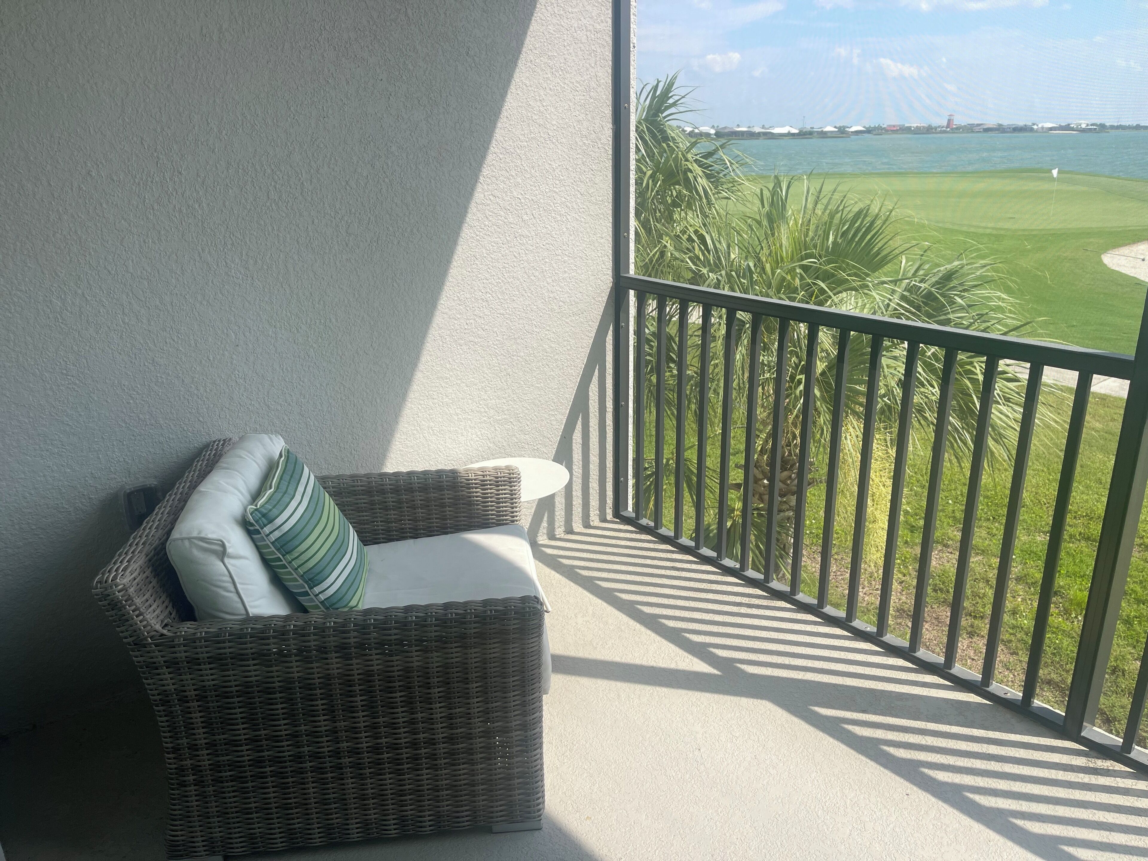 A wicker chair with a cushion and a view of a golf course through a balcony railing.