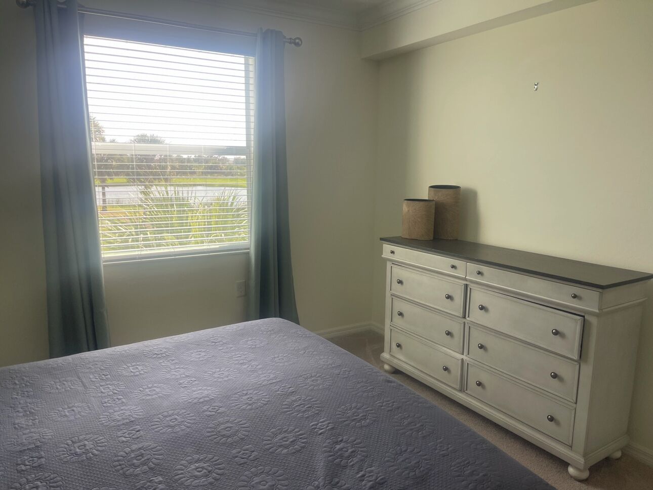 A bedroom with a bed, a dresser, and a window with curtains.