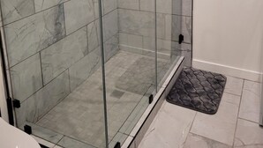 Eine gläserne Dusche mit Marmorboden und einer kleinen Matte im Eingangsbereich.