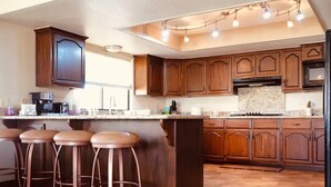 Une cuisine avec des meubles de rangement en bois, un grand îlot central doté de tabourets et un four encastré.