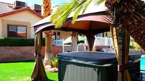 Un bain à remous installé sous une pergola, entouré de palmiers et d’une piscine.