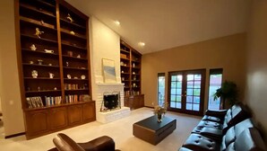 Un salon spacieux avec un canapé en cuir, une table basse et des étagères intégrées remplies de livres et d’objets décoratifs.