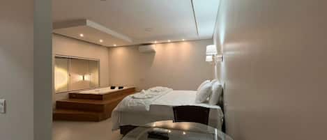 Un dormitorio moderno con una cama, una mesita de vidrio y un banco empotrado.