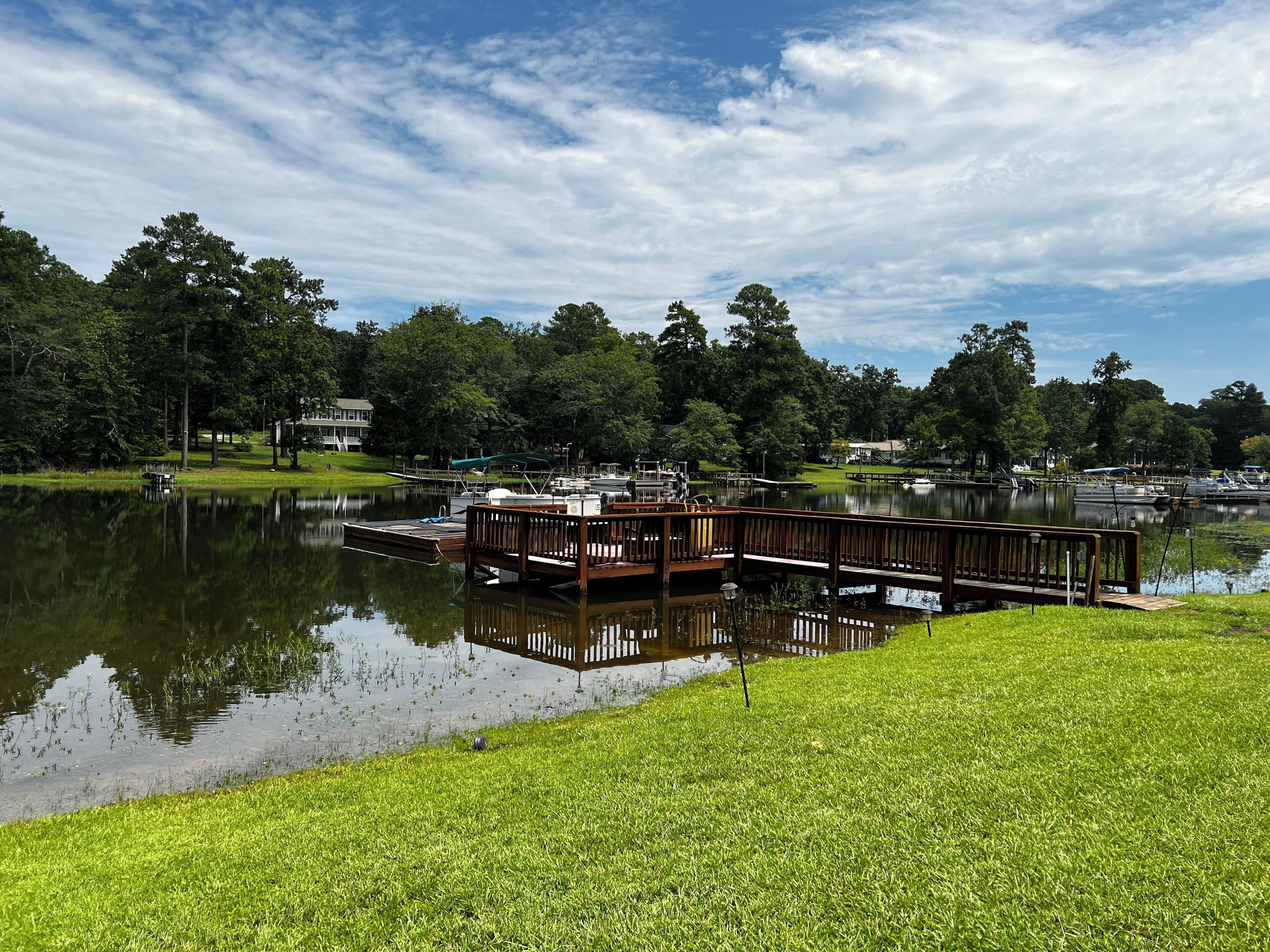 A lakeside dock with a wooden pier, boats, and a grassy area.