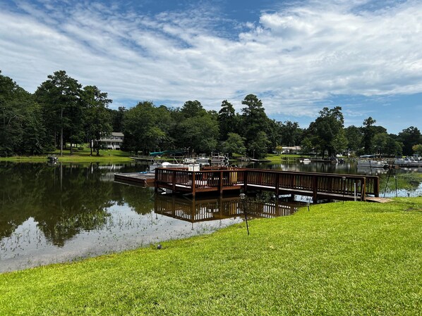 A lakeside dock with a wooden pier, boats, and a grassy area.