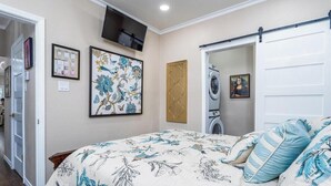 A bedroom with a bed, a television, a washing machine, and a door leading to another room. - Royal Estate Maison Entiere de Luxe (Abilene)