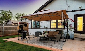Une terrasse extérieure dotée d’un espace salon couvert, d’un barbecue et de plantes en pot.