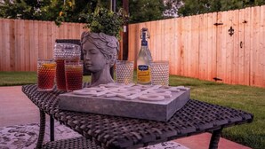 A patio table with a decorative head sculpture, two glasses of beverage, and a bottle of liquor. - Royal Estate Maison Entiere de Luxe (Abilene)