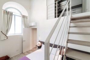 A bedroom with a bed, a nightstand, a lamp, a window with curtains, a staircase, and a dog. - Diaz 8 - MyHomeinComo (Como)