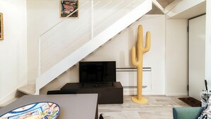 A modern living room with a staircase, a flat-screen TV, a cactus sculpture, and a dining table with a colorful plate. - Diaz 8 - MyHomeinComo (Como)
