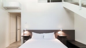 A modern hotel room with a large bed, bedside lamps, a headboard, a small table, and a staircase. - Diaz 8 - MyHomeinComo (Como)