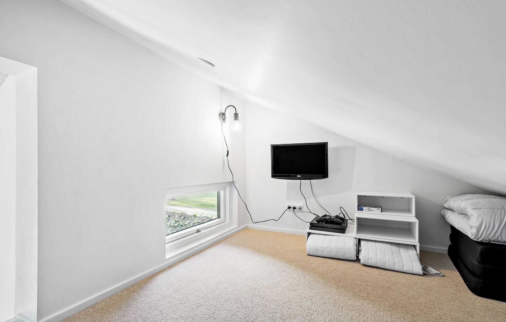 Een kamer met een schuine plafond, een aan de muur bevestigde televisie, een raam met uitzicht en een witte bank.