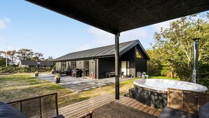 Un espacio al aire libre techado con un jacuzzi, mobiliario de mimbre y una terraza de madera.