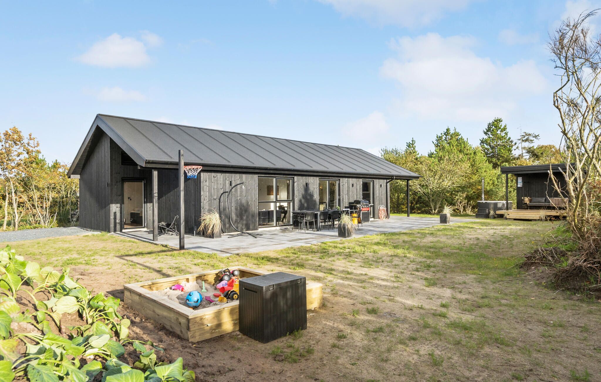 A modern building with a large patio area, a basketball hoop, and a sandbox with toys.