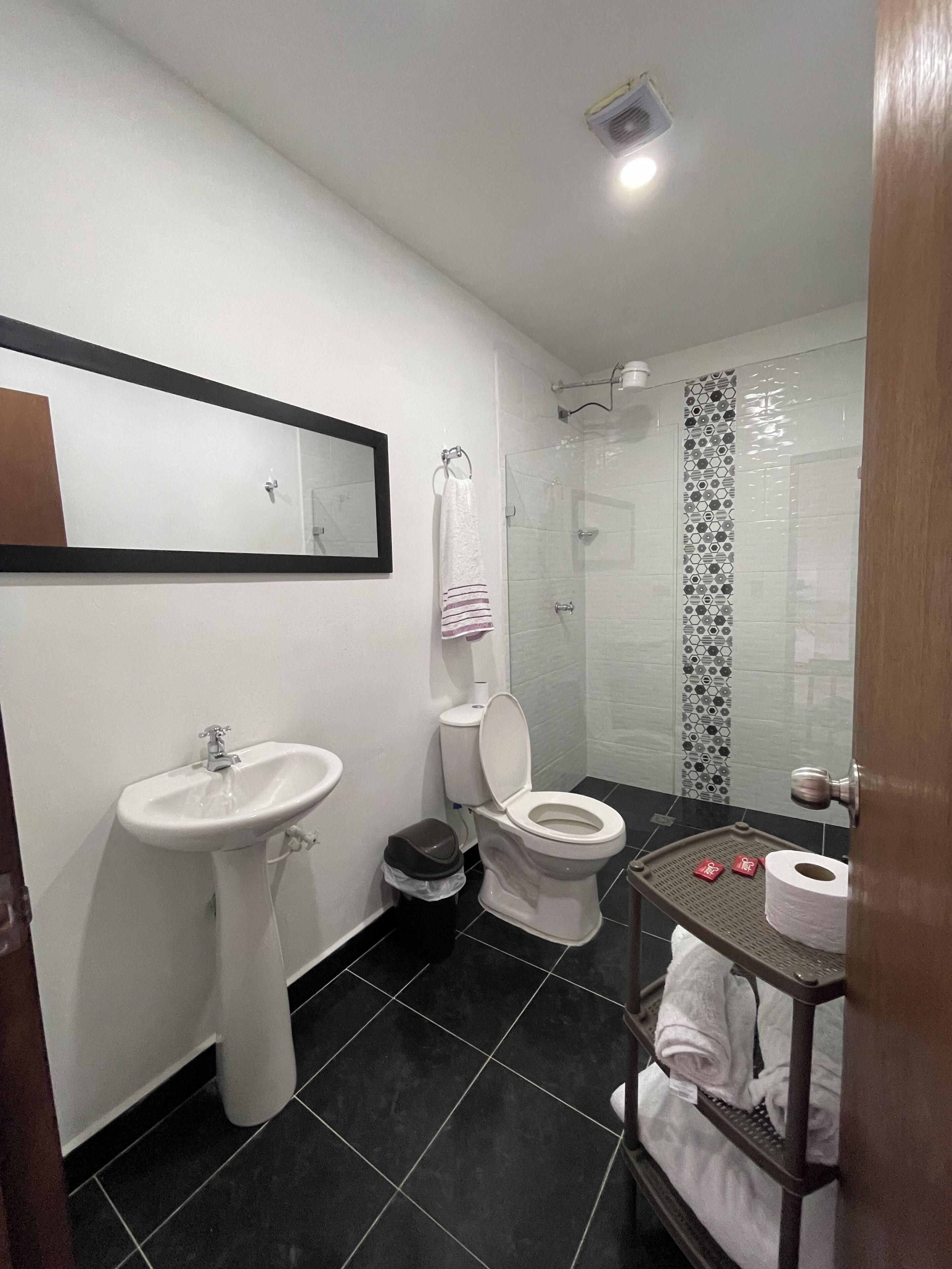 Un baño con lavamanos, inodoro, ducha y un pequeño estante con artículos de aseo.