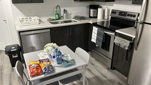 A modern kitchen with a dishwasher, sink, stove, and refrigerator. There is a table with snacks and water bottles. - Cozy and Private Suite - Free On-Prem Parking & PS5 Available (Calgary)