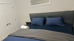 A bedroom with a bed, a nightstand, a towel, and a window with blinds. - Cozy and Private Suite - Free On-Prem Parking & PS5 Available (Calgary)