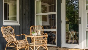 Een houten terras met rieten meubilair en een glazen deur naar een binnenruimte.