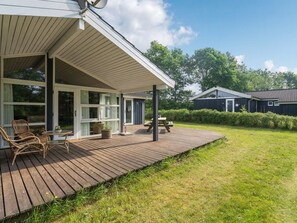 A covered outdoor deck with wicker furniture and a picnic table, adjacent to a building with large windows and a door. - "Anneli" by Interhome (Toftlund)