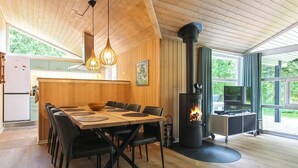 Een moderne keuken met houten kastjes, een eettafel met zwarte stoelen, een houtkachel en een tv op een trolley.