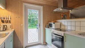 Een keuken met houten wanden, een witte deur die uitkomt op een terras, een magnetron, een oven en een gootsteen.