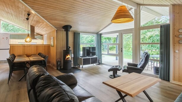 Een moderne woonkamer met een open haard, leren bank, houten eettafel en grote ramen met uitzicht op het groen.