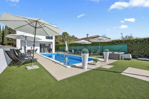 Ein moderner Poolbereich im Freien mit Liegestühlen, Sonnenschirmen und einem gepflegten Rasen.
