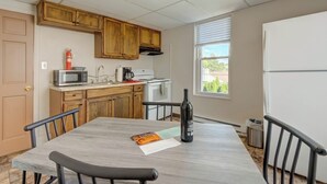 Une cuisine compacte avec des meubles en bois, un four à micro-ondes, une machine à café et une bouteille de vin posée sur la table.