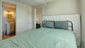 Une chambre à coucher avec un lit, une table de chevet, une lampe et une salle de bain visible à travers une porte ouverte.