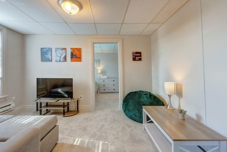 A modern living room with a flat-screen TV, a green bean bag chair, a wooden coffee table, and a white sofa.
