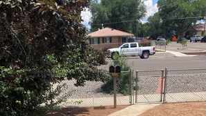 Un vialetto in cemento conduce a una cassetta delle lettere, circondata da una recinzione metallica e alberi.