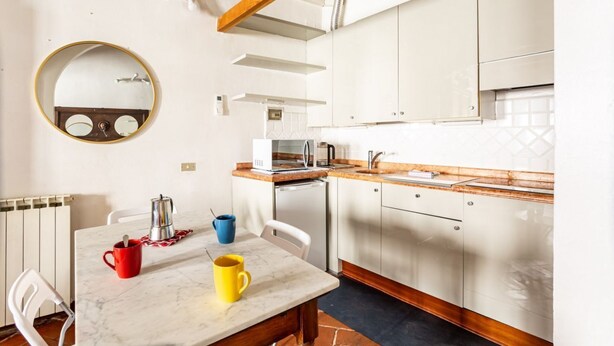 A compact kitchen with white cabinets, a round mirror, a coffee maker, and a table with two mugs. - GuestHost - Archi di San Frediano - Lovely Apartment (Firenze)