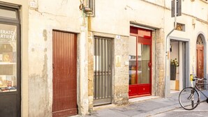 Una calle con un edificio que muestra una tienda cerrada, una puerta marrón, una puerta roja y una bicicleta estacionada afuera.