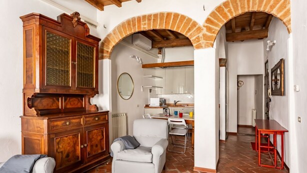 Una habitación con un armario de madera, un sillón blanco, una zona de cocina y una mesa roja.